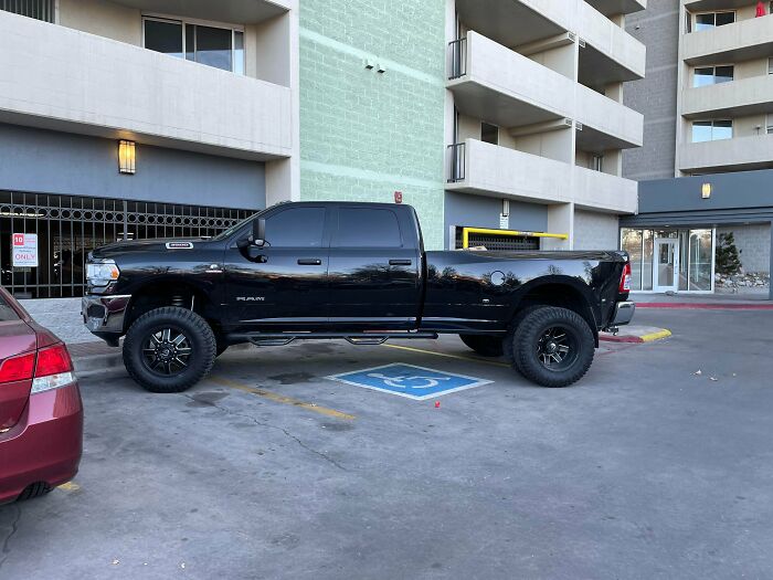 A large black truck parked partially on a handicapped spot, an example of outrageous parking.