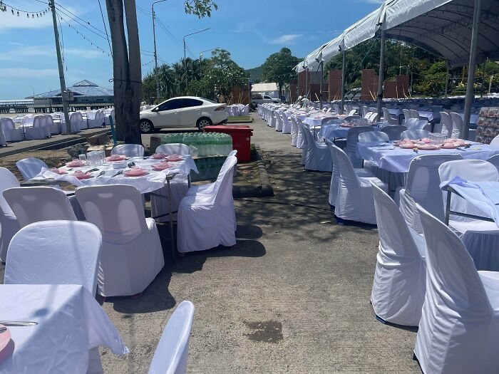 A white car parked among rows of tables under a tent, showcasing outrageous parking in an unexpected location.