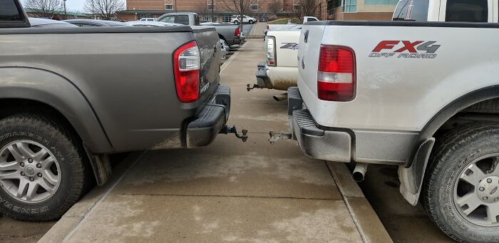 Two pickup trucks parked in a lot, with their rear bumpers almost touching, showcasing outrageous parking.