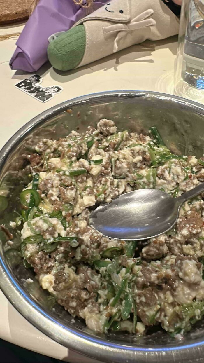 A bowl of disgusting food, featuring a mix of meat, cheese, and green vegetables.