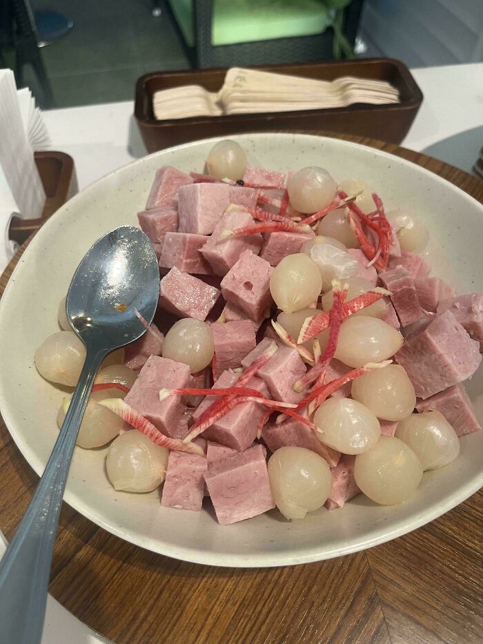 A bowl of disgusting food featuring cubed pink meat and small white pickled onions, deserving public shame.
