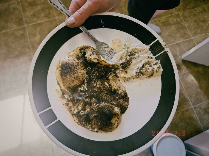 A plate with a burnt, blackened chicken breast next to mashed potatoes, a piece of stupid and disgusting food.