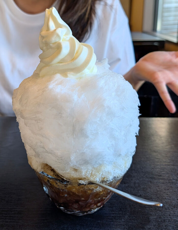 A large glass of disgusting food, specifically a shaved ice dessert topped with soft serve, on a table.