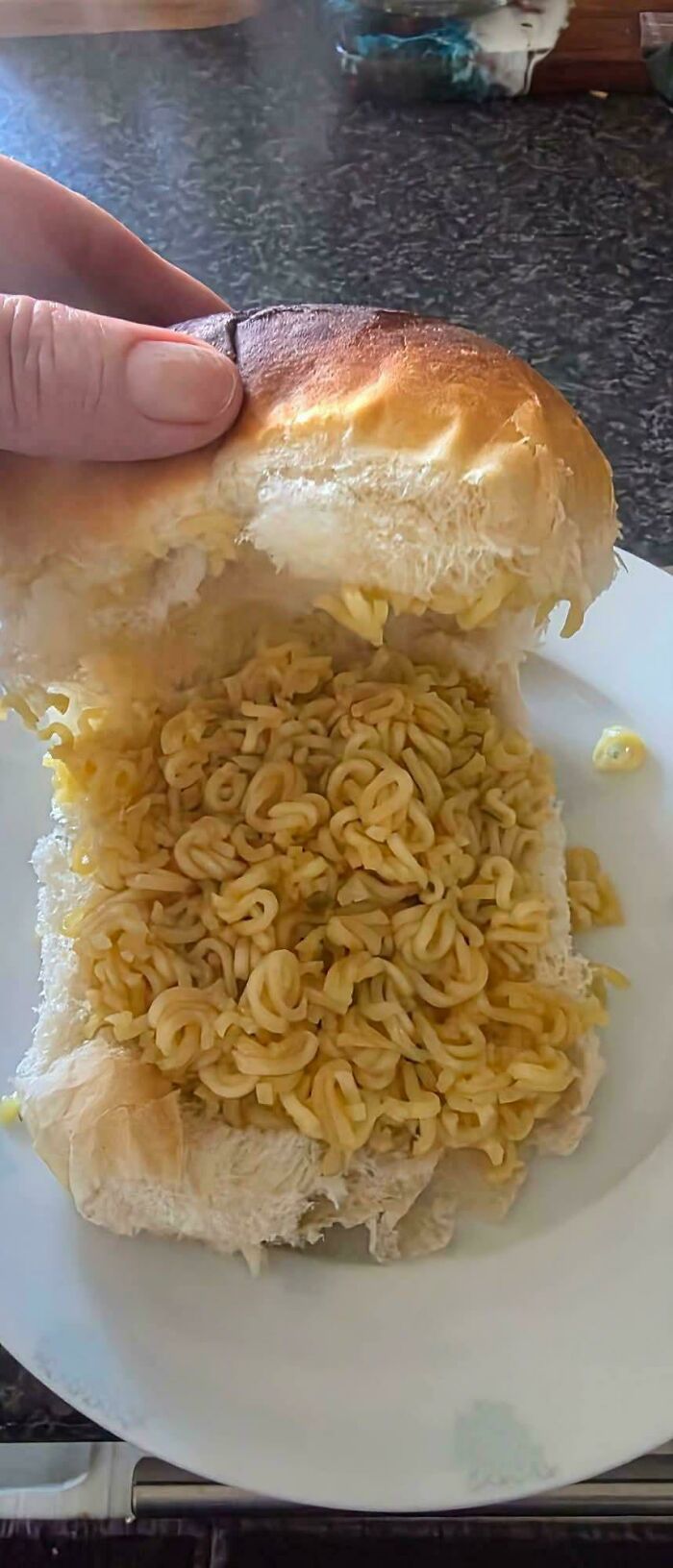 A close-up of a bread bun filled with instant ramen noodles, an odd and disgusting food combination.
