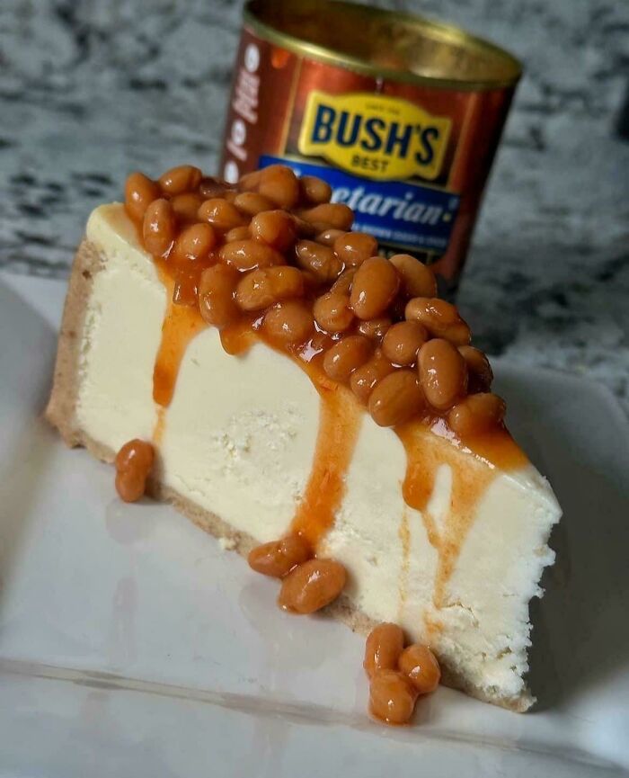 A slice of cheesecake topped with baked beans, a prime example of stupid and disgusting food served on a white plate.