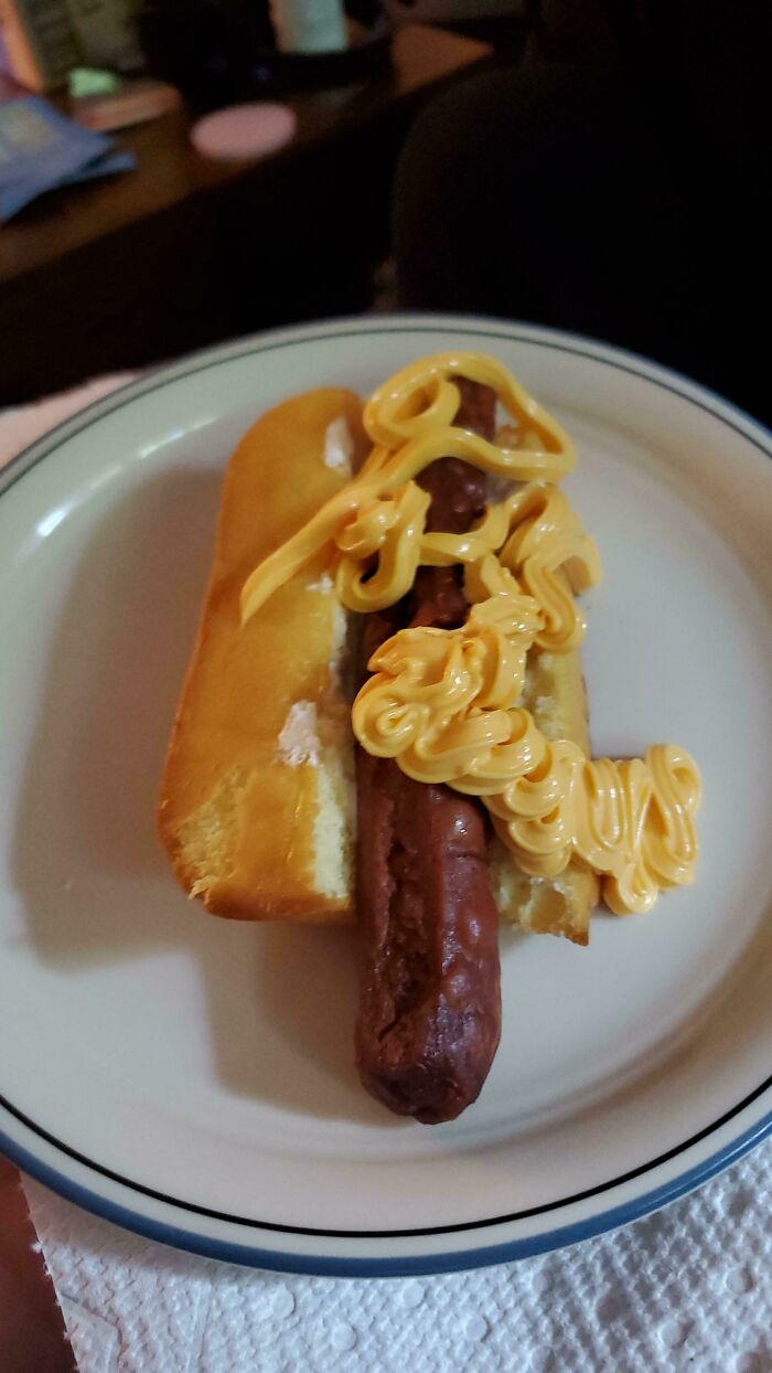 A hot dog in a bun with copious amounts of yellow mustard, an example of stupid and disgusting food.