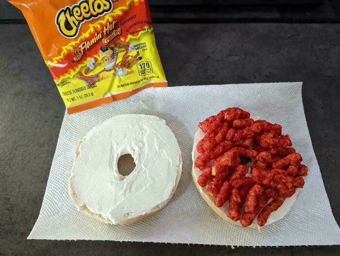 An open bagel with cream cheese and Flamin Hot Cheetos, a stupid and disgusting food creation.