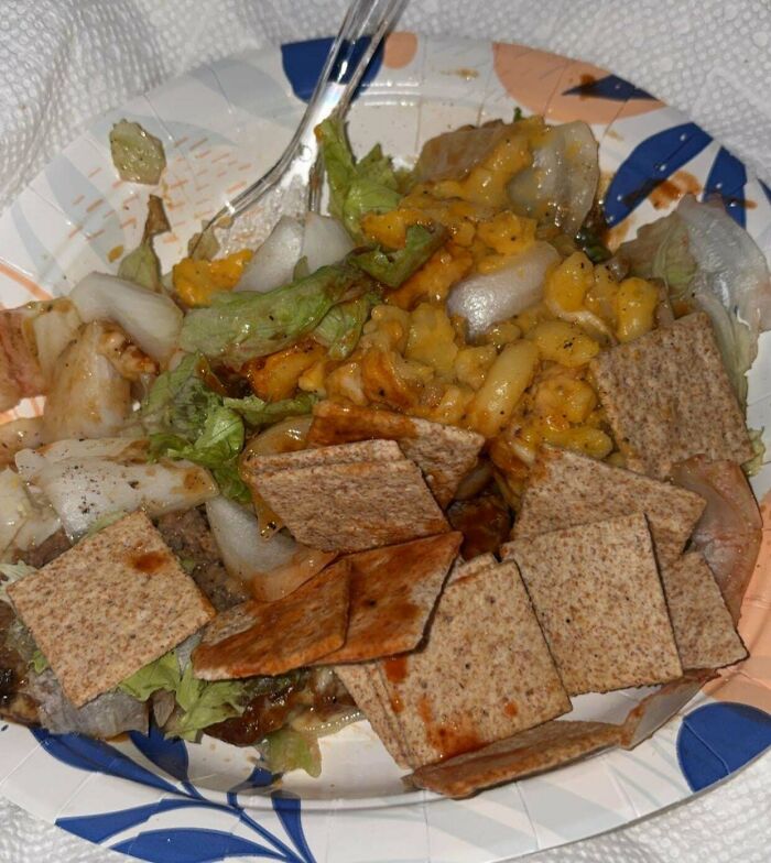 A paper plate with a messy mix of disgusting food, including lettuce, onions, and crackers.