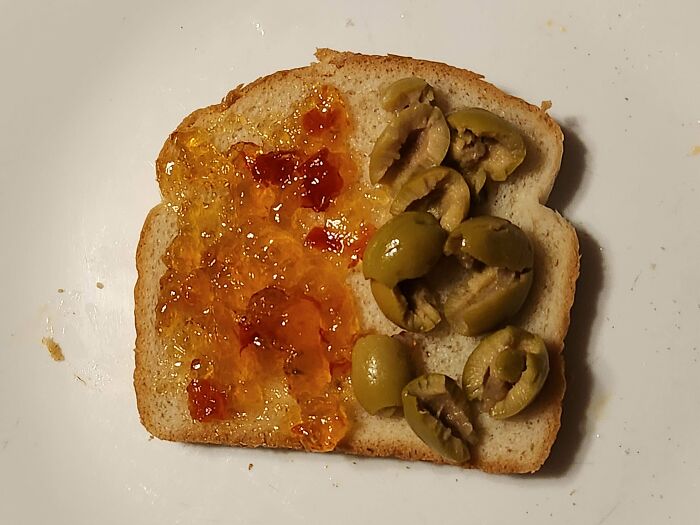 A slice of bread topped with jam on one side and olives on the other, a stupid and disgusting food combination.