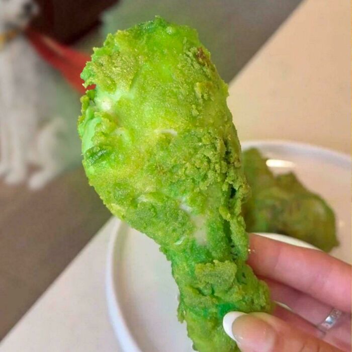 A hand holding a bright green, oddly textured chicken drumstick, an example of stupid food.