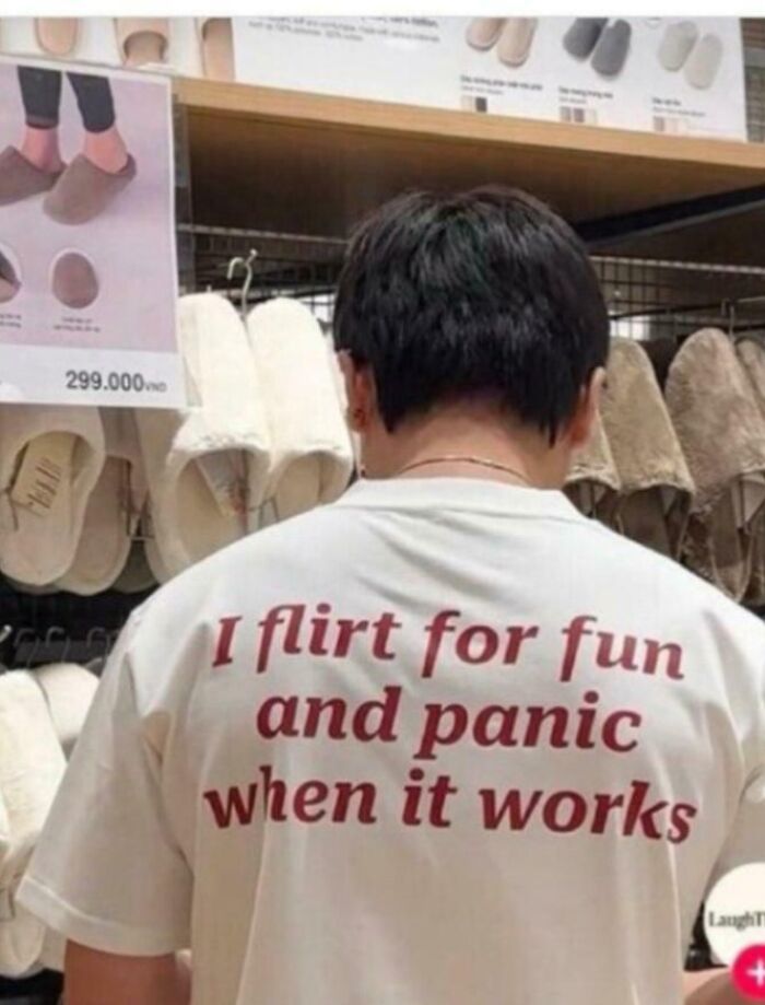 A person wearing a white shirt with a funny sentence, standing in an aisle with slippers. Unpredictable sentences often feature humor.