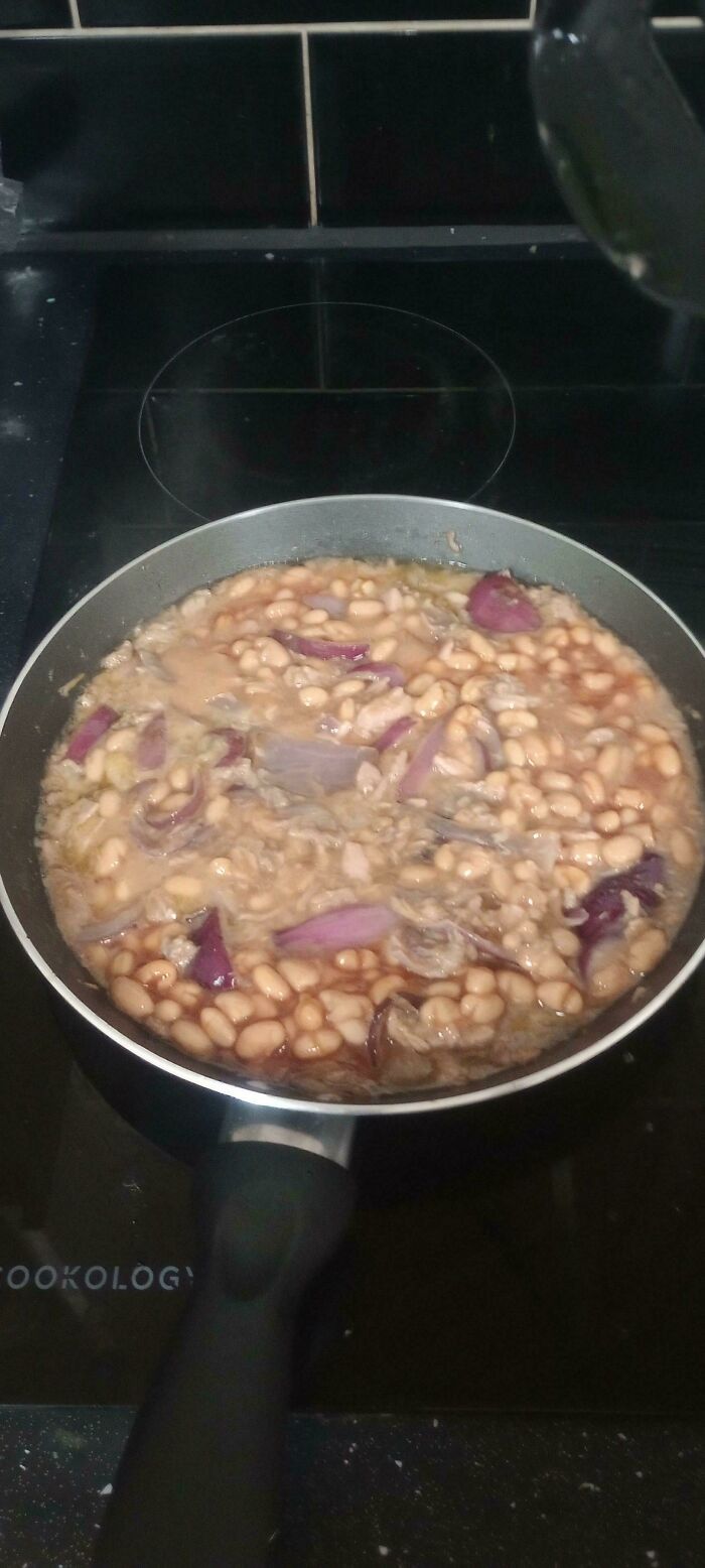 Disgusting food in a frying pan, showing white beans and large pieces of red onion simmering in liquid.