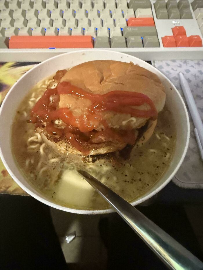 Stupid food featuring a burger submerged in a bowl of ramen noodles, an odd and unappetizing combination.