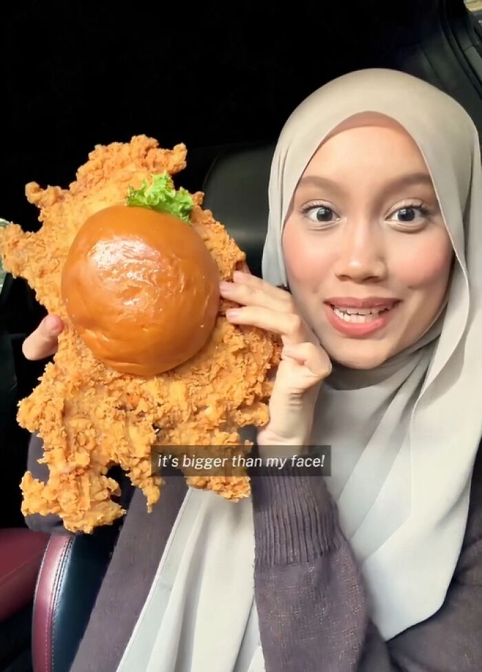 A woman holding an enormous fried chicken sandwich, highlighting the scale of this disgusting food.