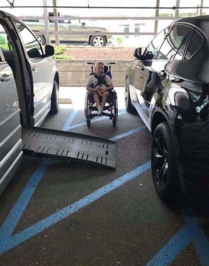 A young boy in a wheelchair smiles as two cars are parked too close, blocking his accessible ramp due to outrageous parking.