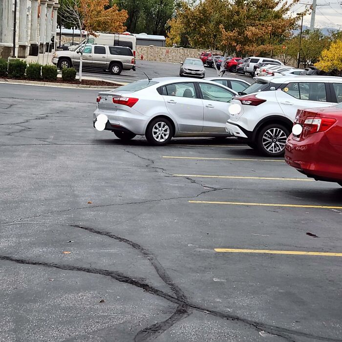 Multiple cars are parked haphazardly in a lot, with one silver car exhibiting particularly outrageous parking.