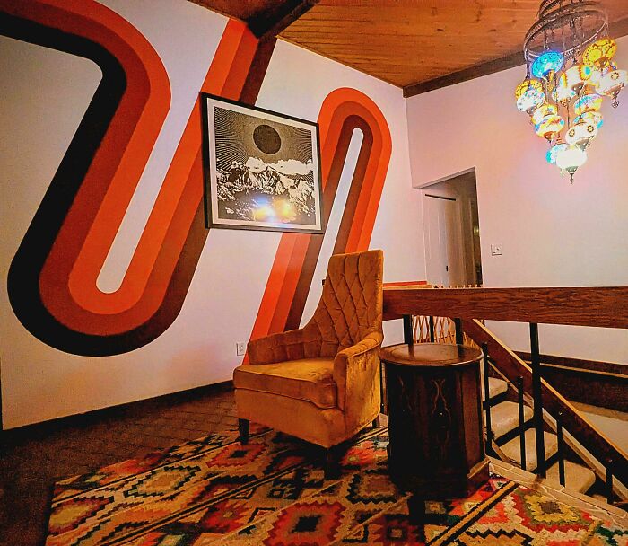 A cozy corner with a mustard yellow armchair and a retro striped wall, reflecting 1970s and 1980s interior design.