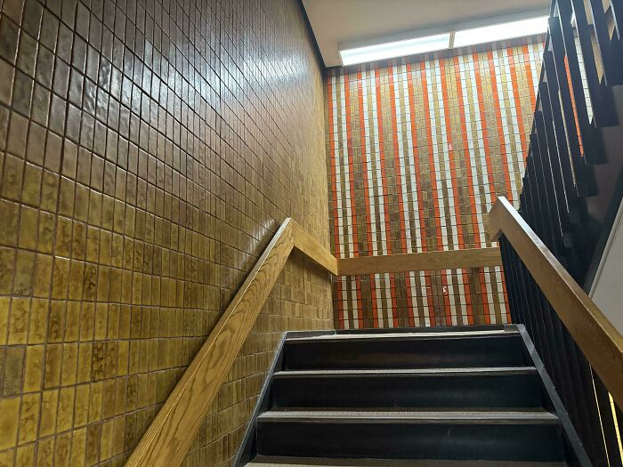 Staircase with brown tiled walls and a striped accent wall featuring orange, white, and brown, characteristic of 1970s and 1980s interior design.
