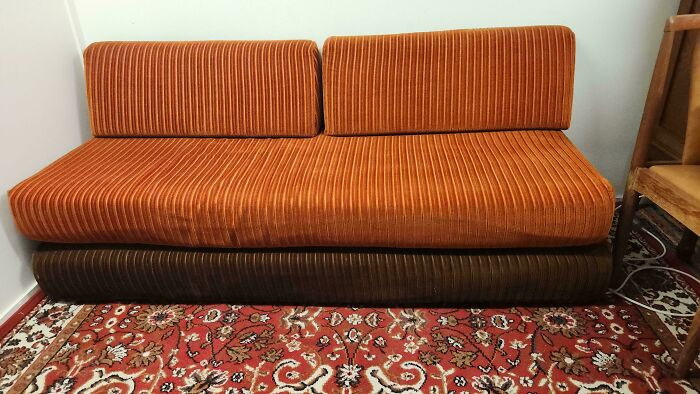 An orange corduroy sofa on a patterned rug, epitomizing 1970s and 1980s interior design.