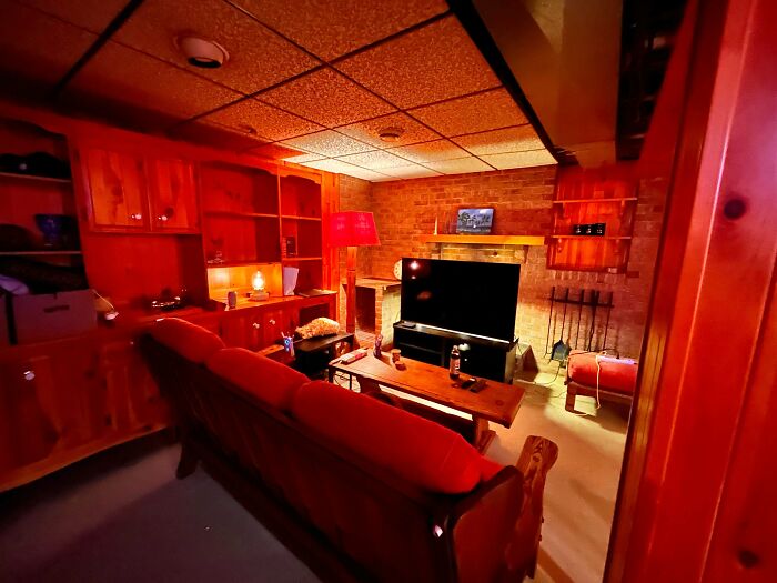 A cozy 1980s interior design living room bathed in red light, featuring a brick fireplace and a long red sofa.