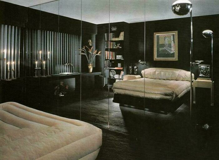 A luxurious 1970s and 1980s interior design bedroom with dark walls, a large bed, mirrored closet doors, and modern lighting.