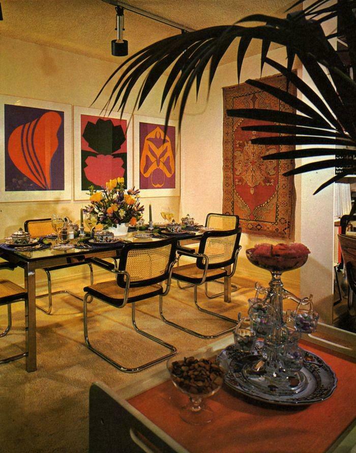 A sophisticated dining room with modern art, a set table, and lush greenery represents 1970s and 1980s interior design.