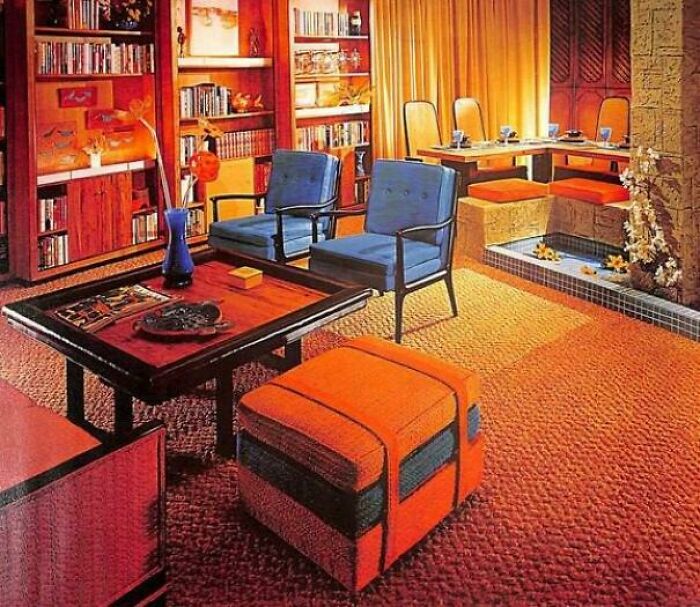 A vibrant 1970s and 1980s interior design living room with orange carpet, blue chairs, and built-in bookshelves.