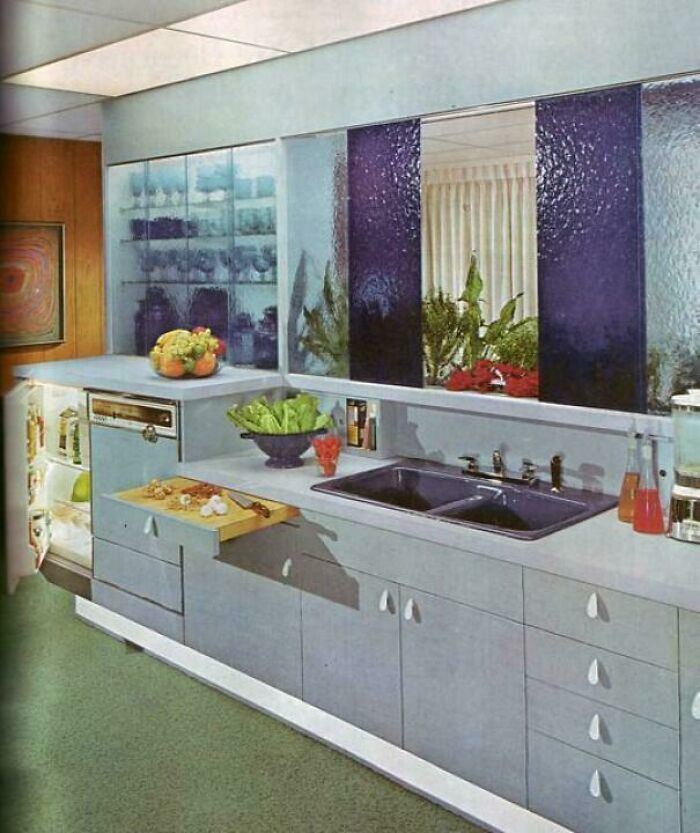 A 1970s and 1980s interior design kitchen featuring a dual sink, fresh produce, and unique purple glass paneling.
