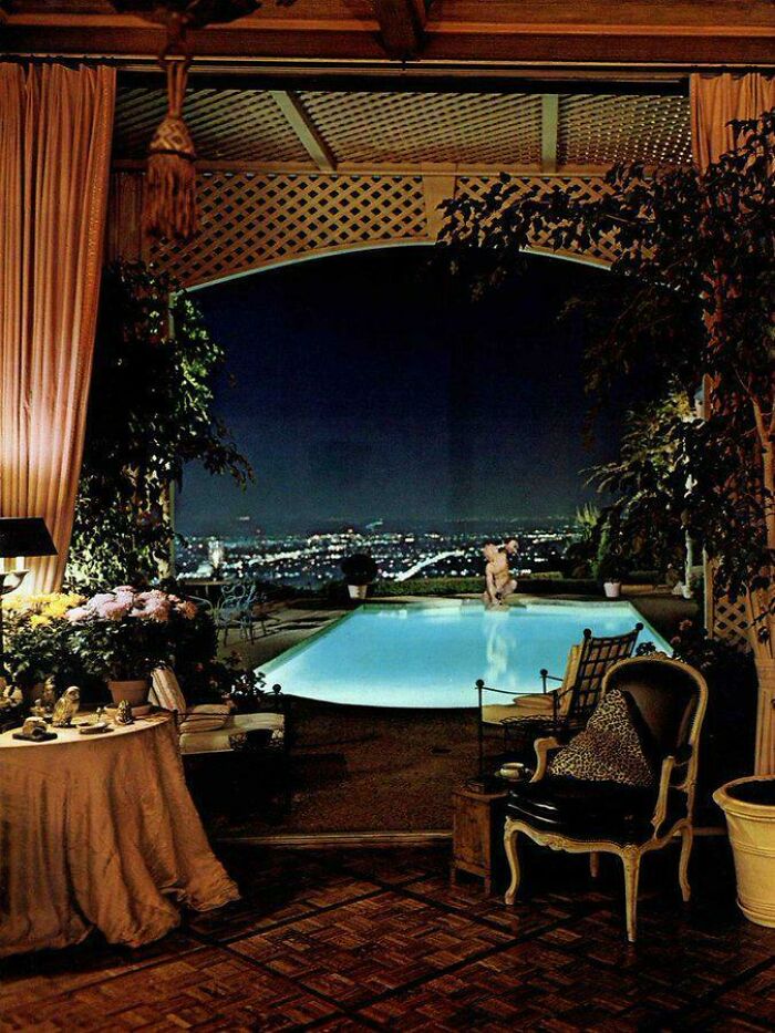 A sophisticated poolside patio with city views at night, reflecting 1970s and 1980s interior design luxury.