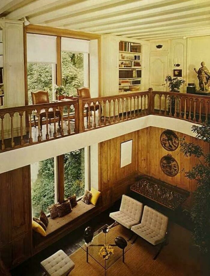 A split-level 1970s interior design room with wood paneling, large windows, and a sitting area with plush sofas.