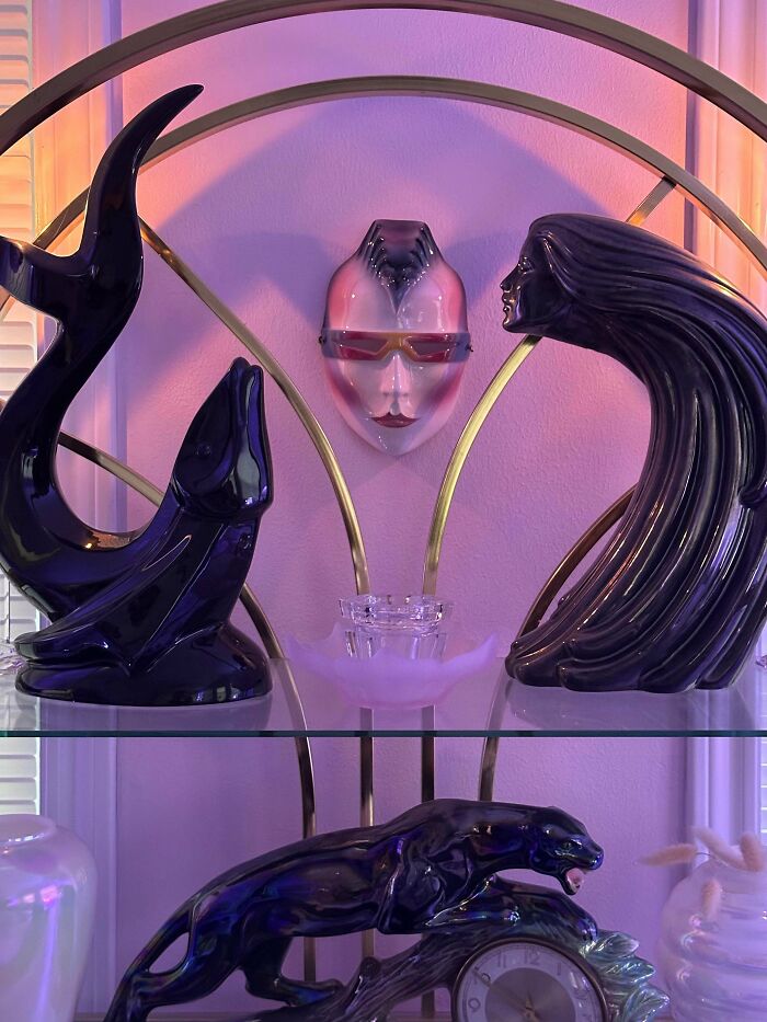 Decorative ceramic sculptures and a face mask embodying 1980s interior design aesthetics on a display shelf.