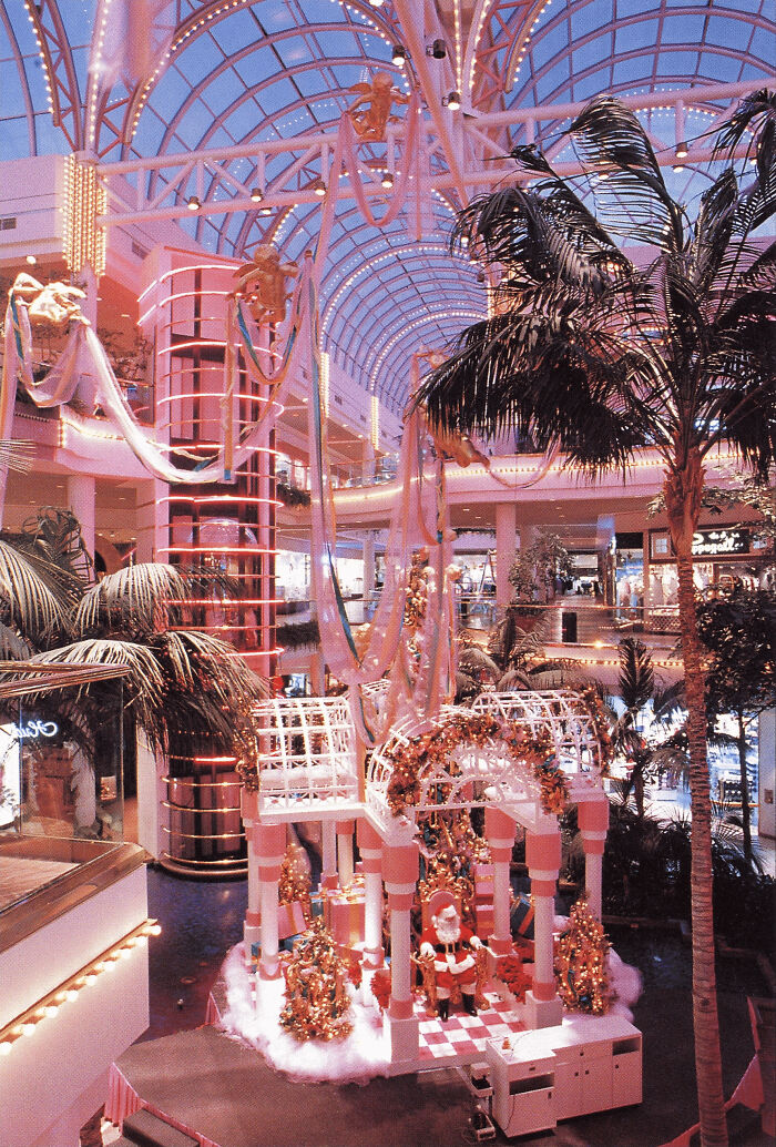 A shopping mall with pink lights and Christmas decorations, capturing 1970s and 1980s interior design.