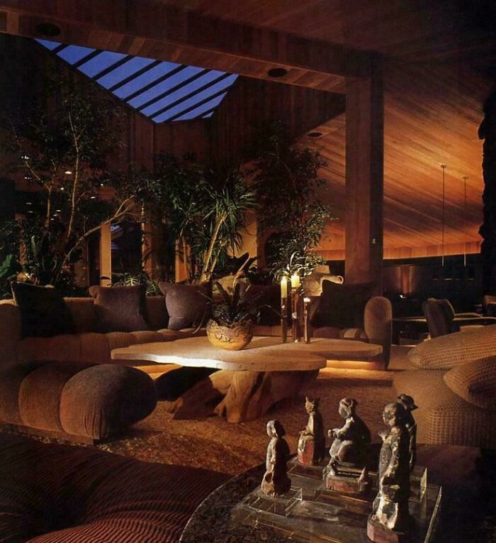 A sprawling 1970s interior design living room with a large stone coffee table, plants, and a skylight.
