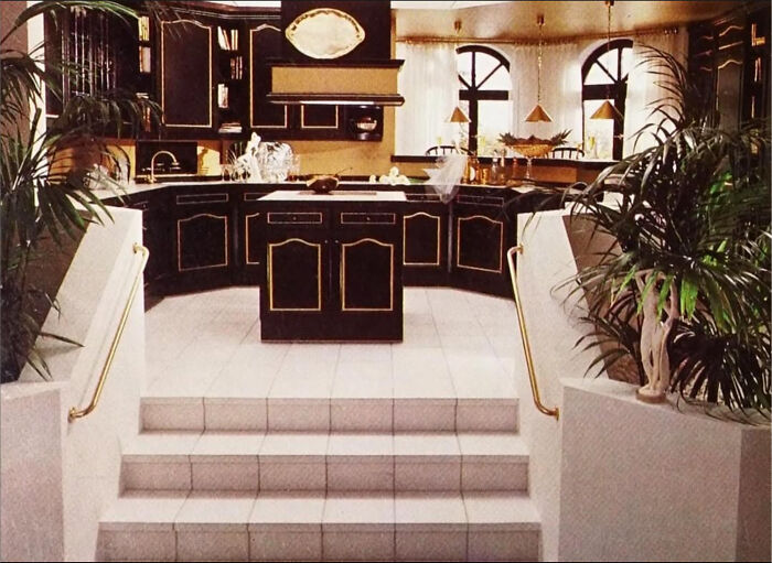A luxurious 1980s interior design kitchen with black and gold cabinetry, an island, and large arched windows.