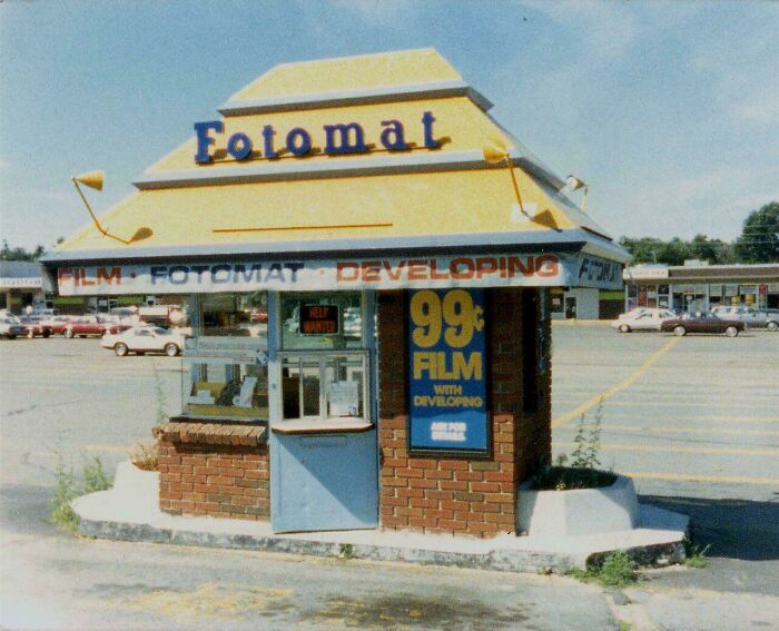 A Fotomat booth in a parking lot, an iconic piece of 1970s and 1980s history, offering film developing services.