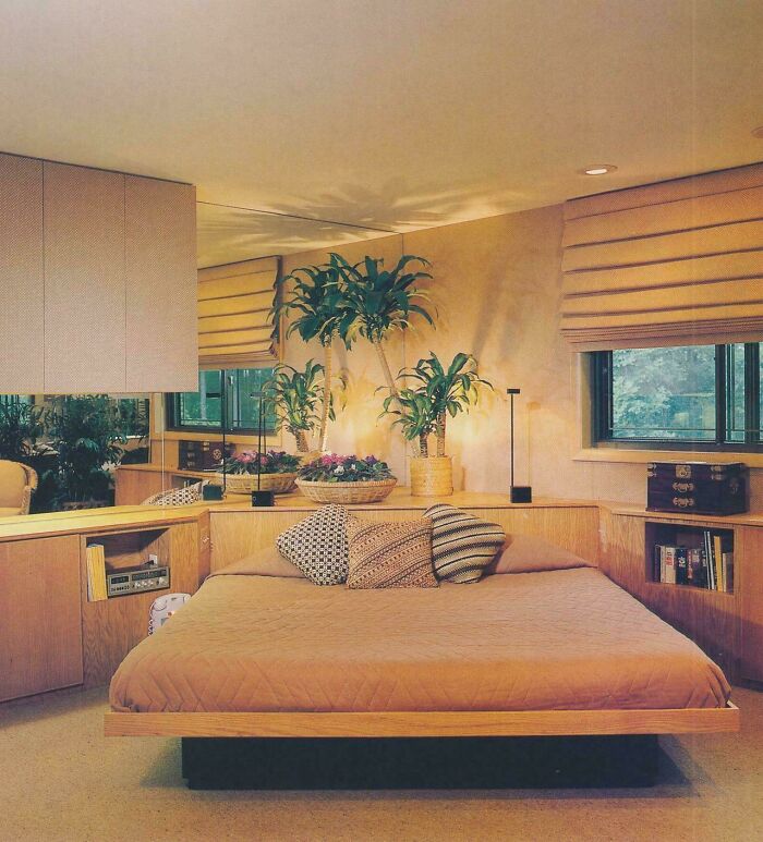 A cozy 1980s interior design bedroom featuring a low-set bed, built-in shelves, and potted plants.