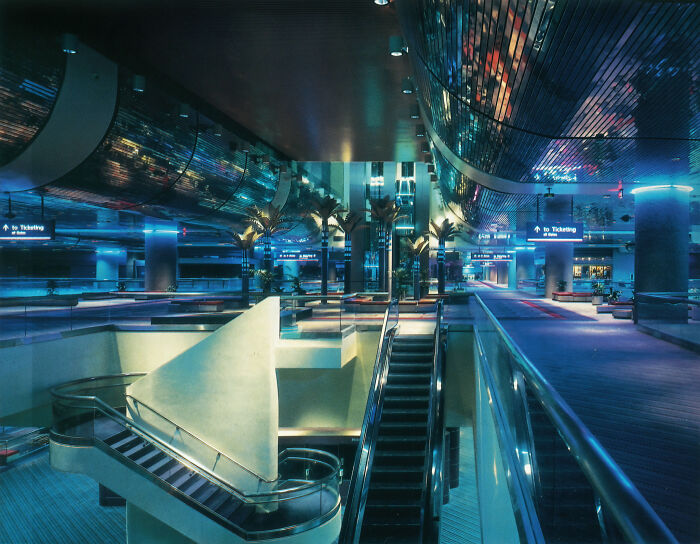 A sprawling 1980s interior design airport terminal with bright blue lighting and palm trees.