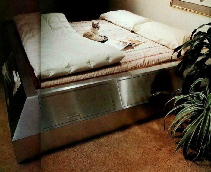 A bedroom with a sleek, low-profile bed, a cat, and a plant, embodying 1970s and 1980s interior design.