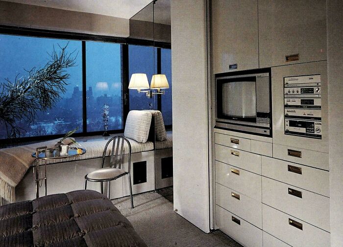 A room with a large window and built-in storage, displaying 1970s and 1980s interior design elements and a vintage entertainment system.