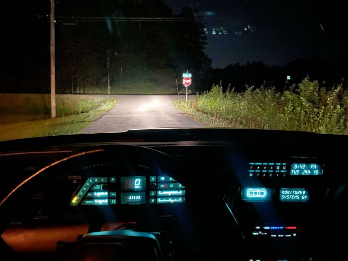 A car's dashboard at night with glowing digital displays, reflecting 1970s and 1980s interior design.