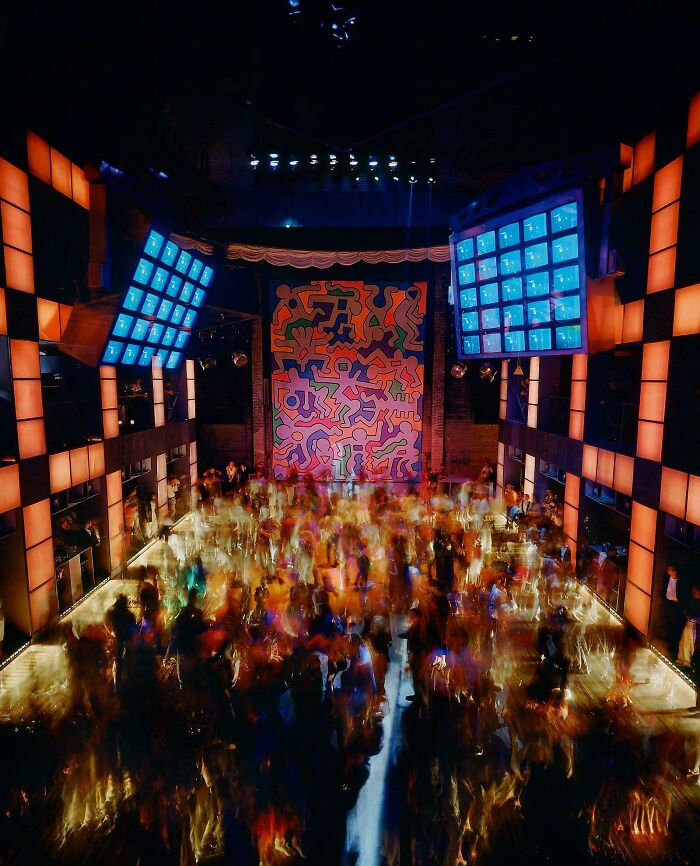 A vibrant 1980s interior design nightclub with a colorful Keith Haring mural and a crowded dance floor, full of energy.