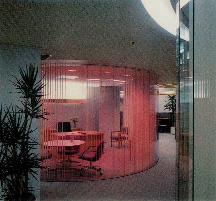 An office meeting room featuring bold 1980s interior design, with curved pink translucent walls and modern furniture.