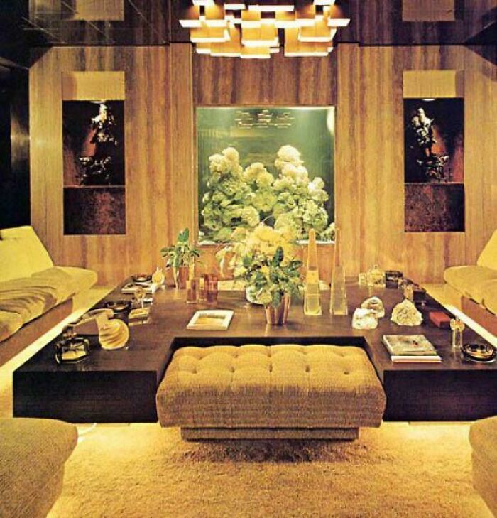 A luxurious 1970s interior design living room featuring a large central table, plush seating, and an illuminated aquarium.