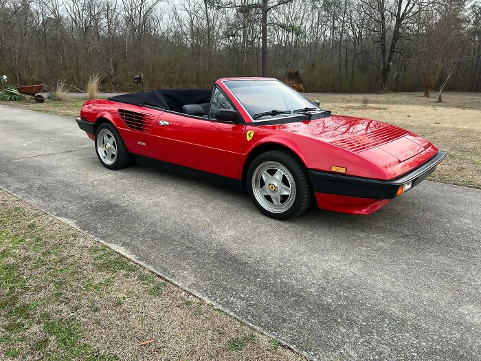 A red 1980s car, a Ferrari Mondial cabriolet, representing classic 1980s design.