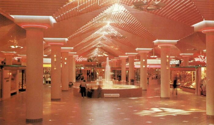 A spacious 1980s interior design of a mall atrium with a central fountain and warm lighting, capturing the era.