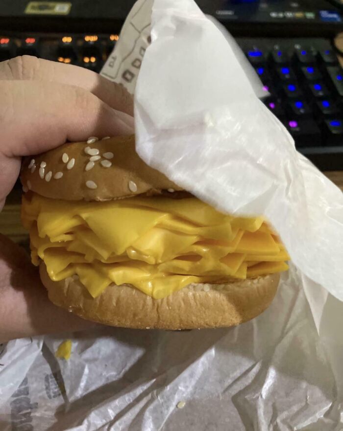 A hand holding a stupid and disgusting food sandwich with many layers of cheese.