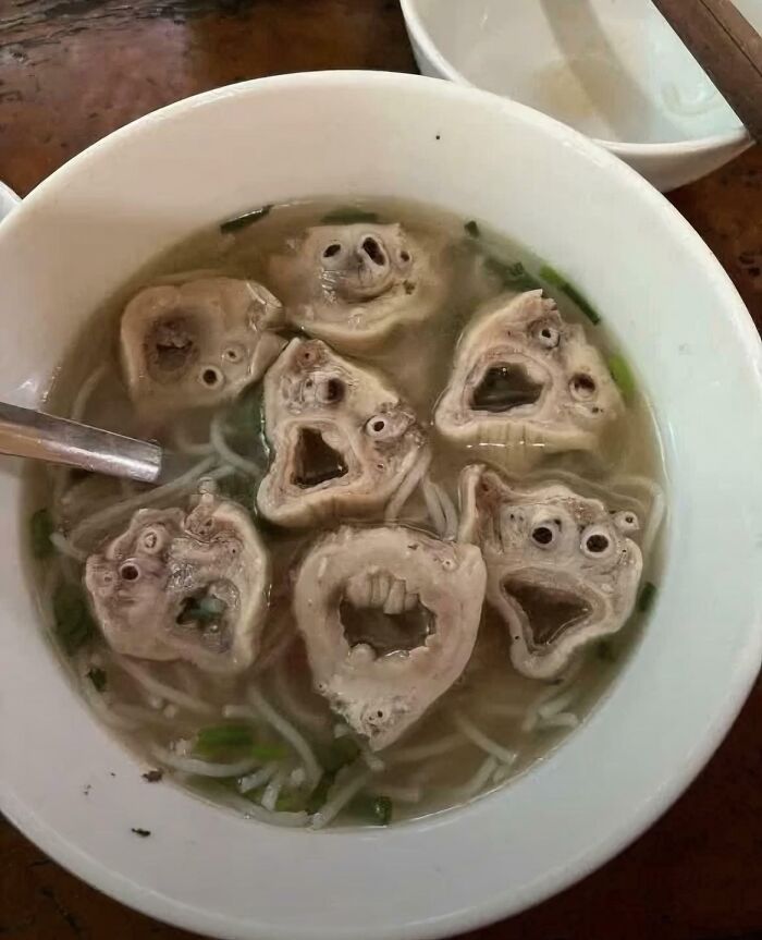 Disgusting food in a bowl, a soup with several creepy, distorted meat pieces resembling faces.