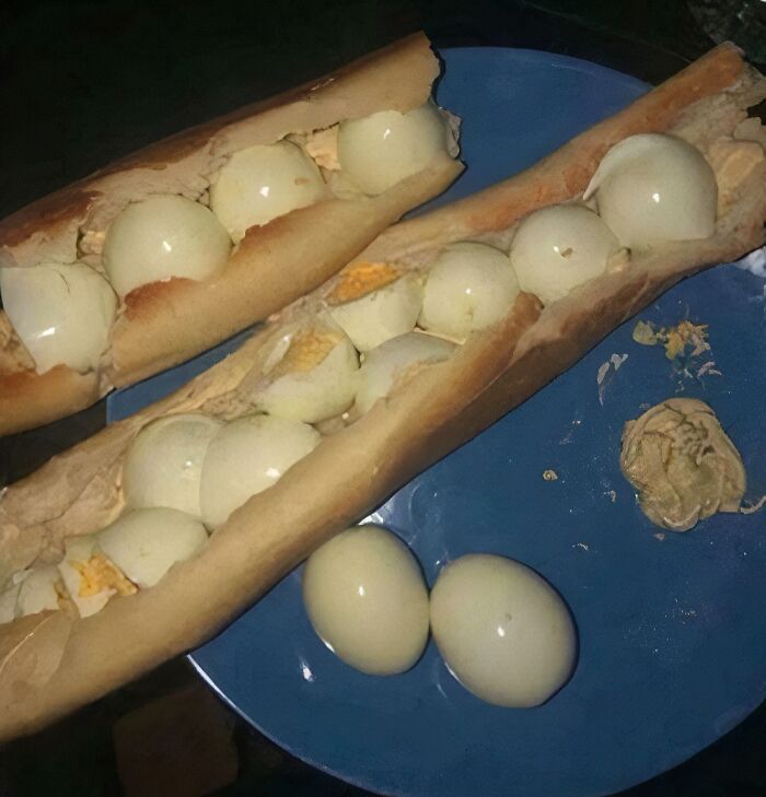 Two baguettes filled with numerous hard-boiled eggs on a blue plate, a piece of stupid and disgusting food.