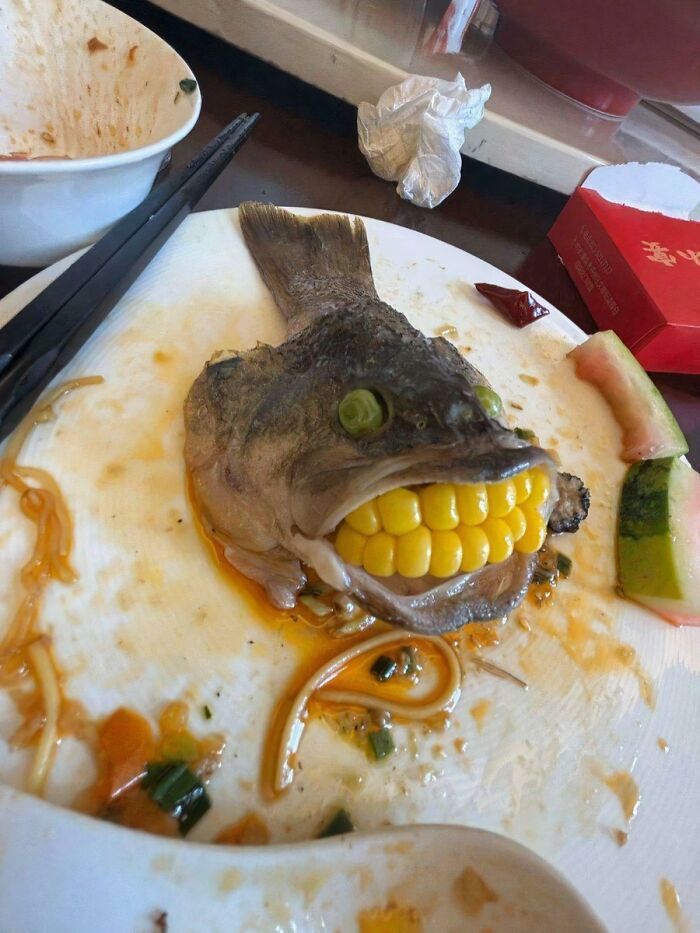 A fish head with corn kernels as teeth on a messy white plate, representing disgusting food.