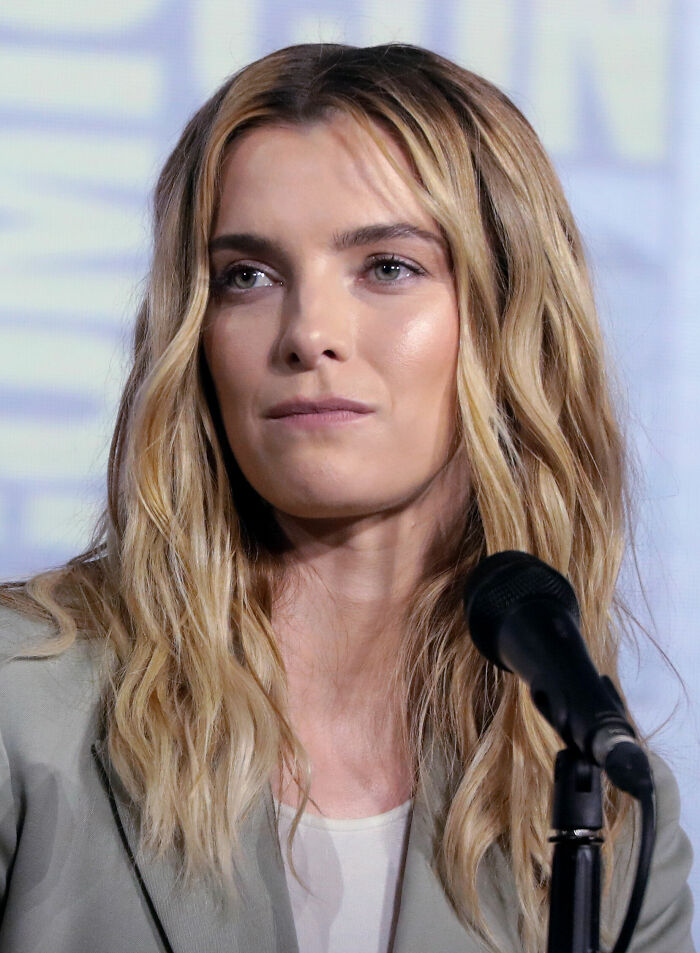 A close-up shot of Betty Gilpin, an American actress known for her career highlights, speaking at a microphone.
